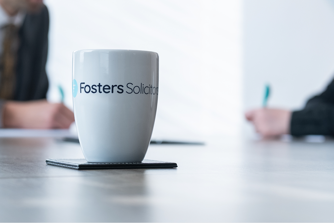 Fosters Solicitors mug on a table with clients in the background