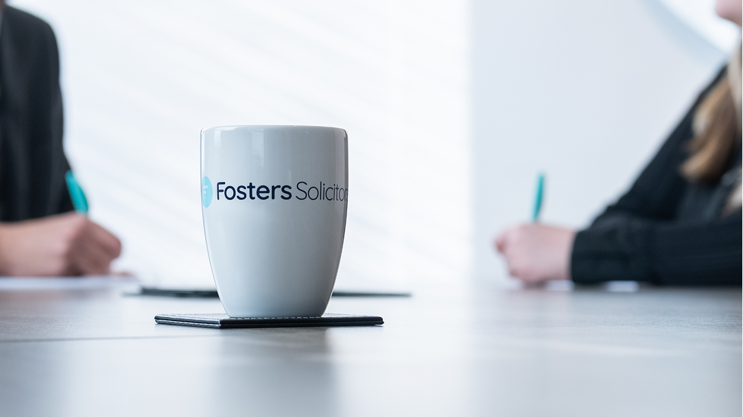 Fosters Solicitors mug on a table with a colleague writing notes in the background