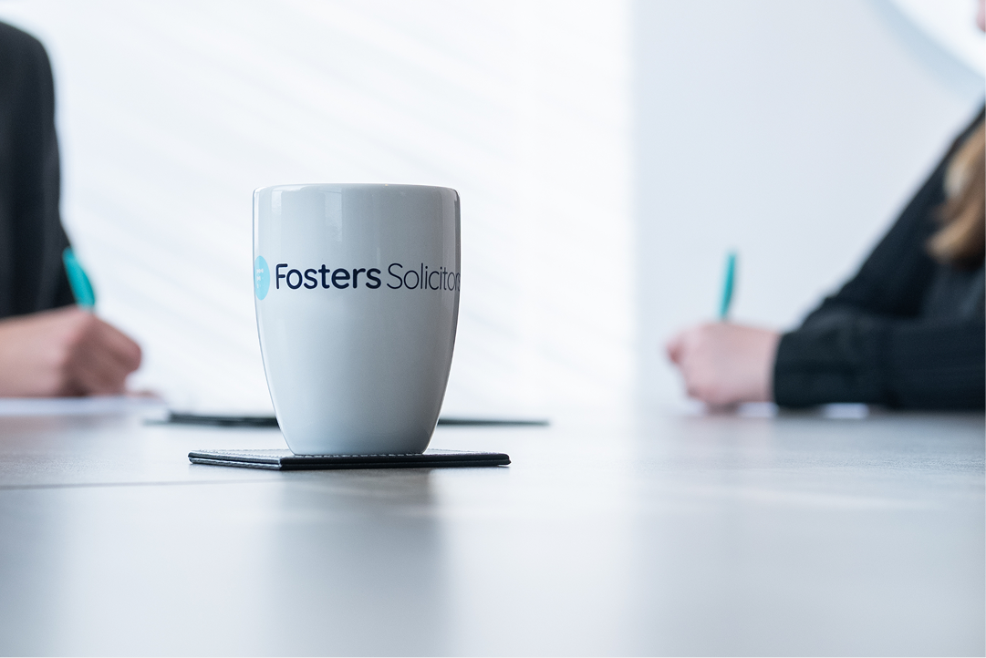 Fosters Solicitors mug on a table with clients writing on either side