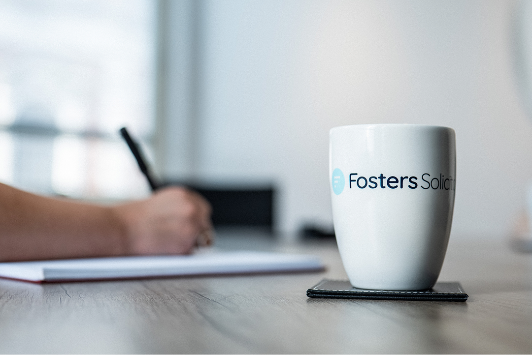 Fosters Solicitors mug on a table with a client writing in the background