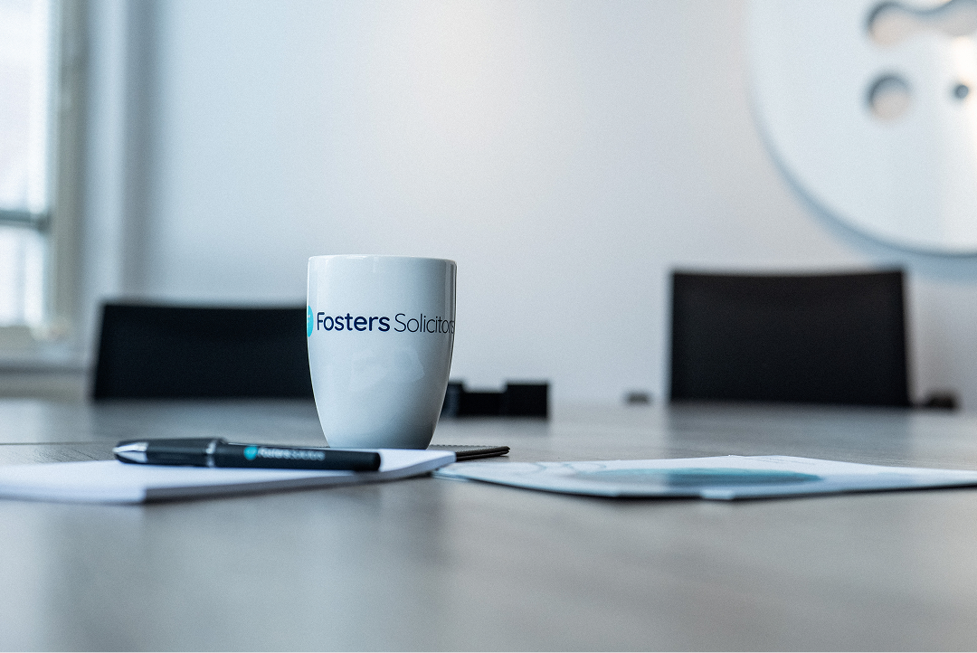 Fosters Solicitors mug and pen on a boardroom table with papers