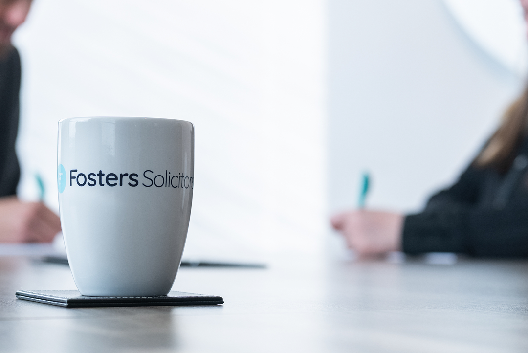 Fosters Solicitors mug on a table with clients writing in the background