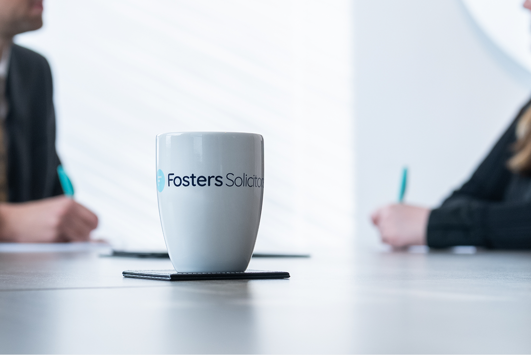 Fosters Solicitors mug on a table with clients in the background