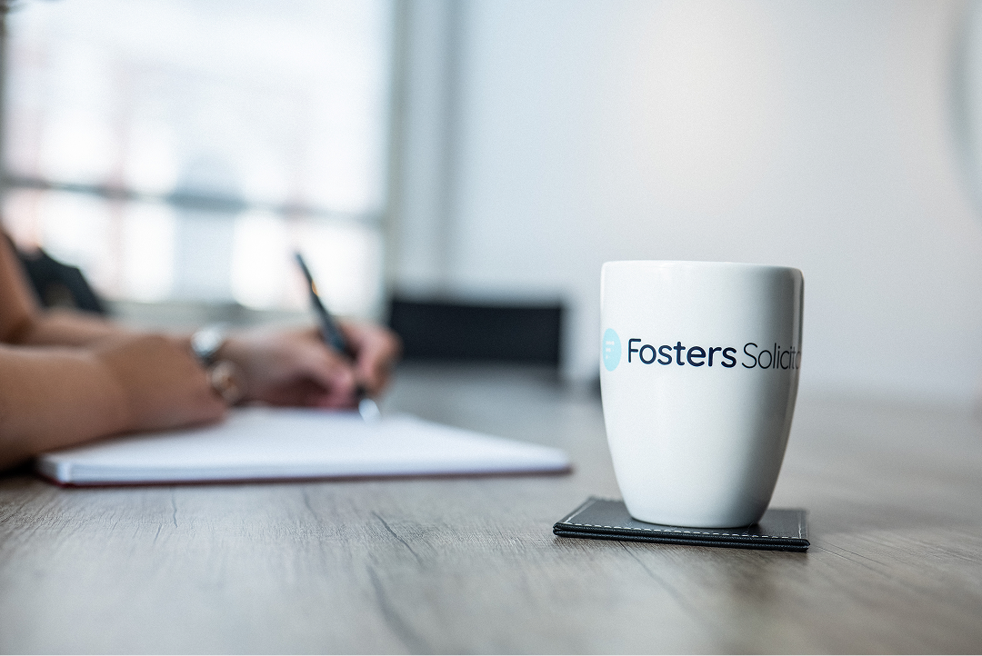Fosters Solicitors mug on a table with a colleague writing notes in the background