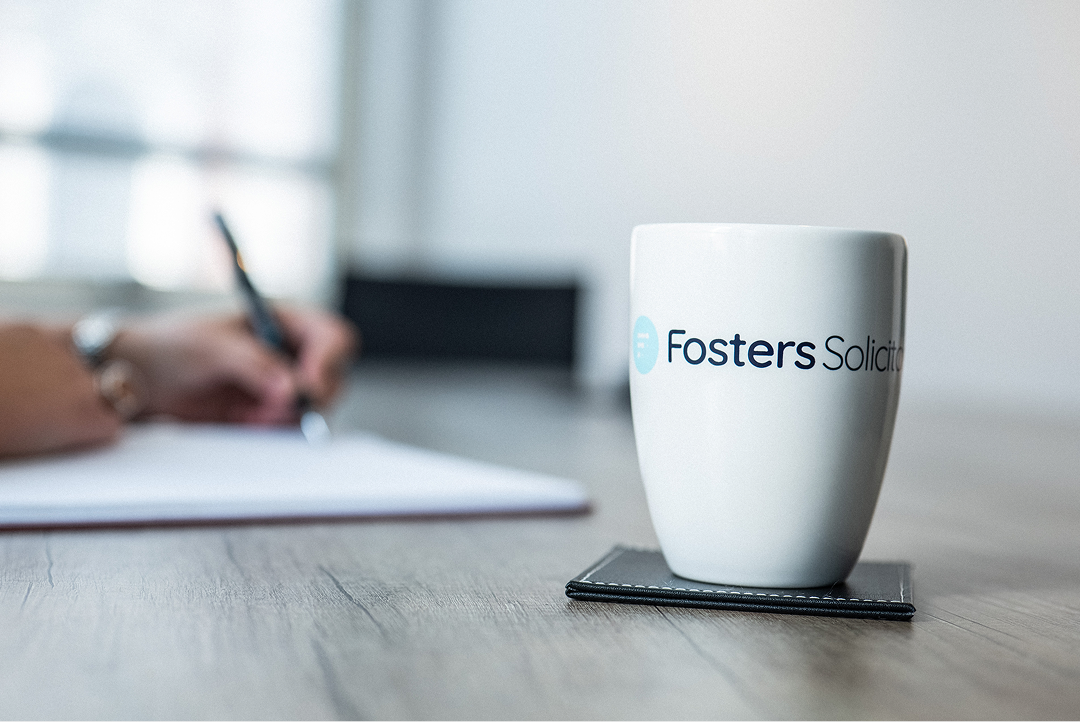 Fosters Solicitors mug on a table with a colleague writing notes in the background