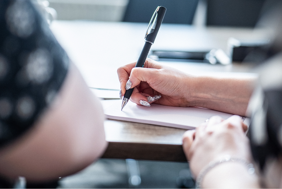 Close-up of a hand writing with a pen at a desk