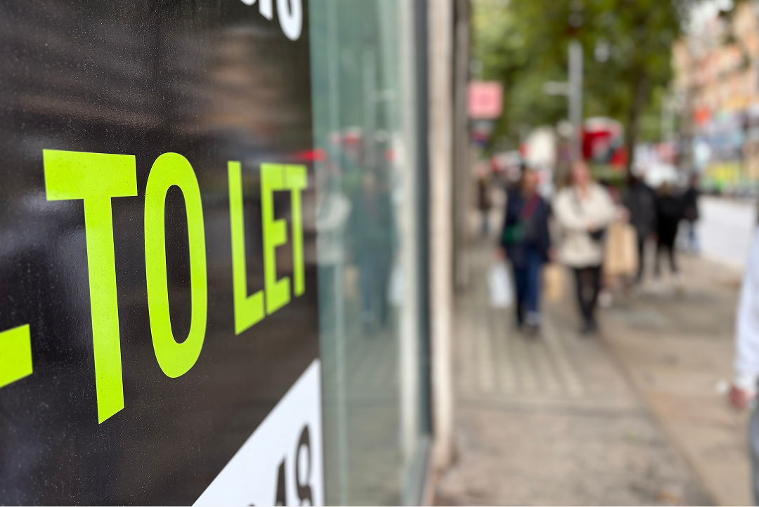 Close-up of a To Let sign on a shopfront with pedestrians in the background