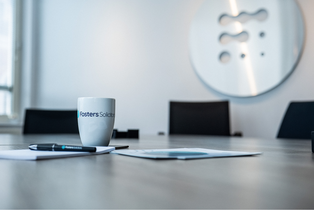 Fosters Solicitors mug on a boardroom table with a decorative wall panel in the background