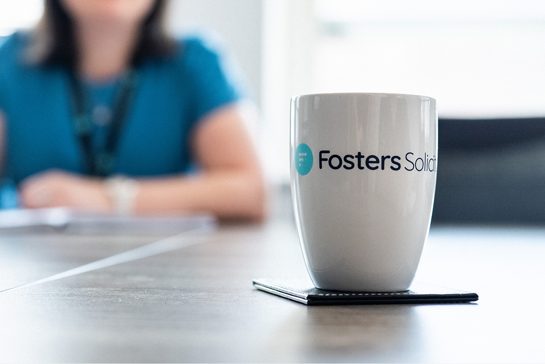 Fosters Solicitors mug on a table with a client wearing a lanyard in the background