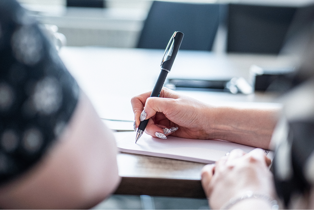 Close-up of a hand writing with a pen at a desk
