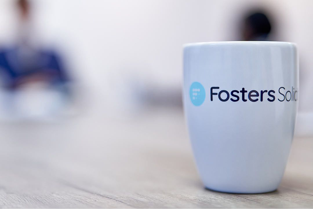 Fosters Solicitors mug on a table with clients in the background