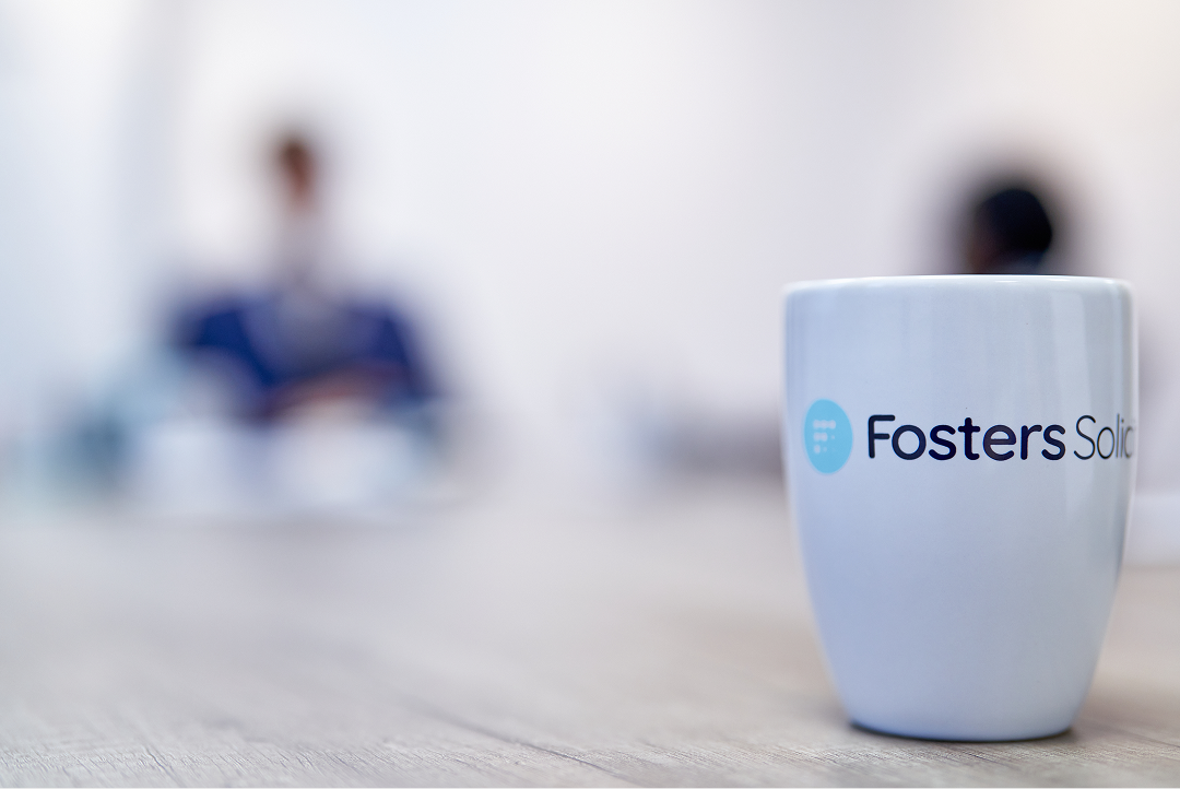 Fosters Solicitors mug on a table with clients in the background