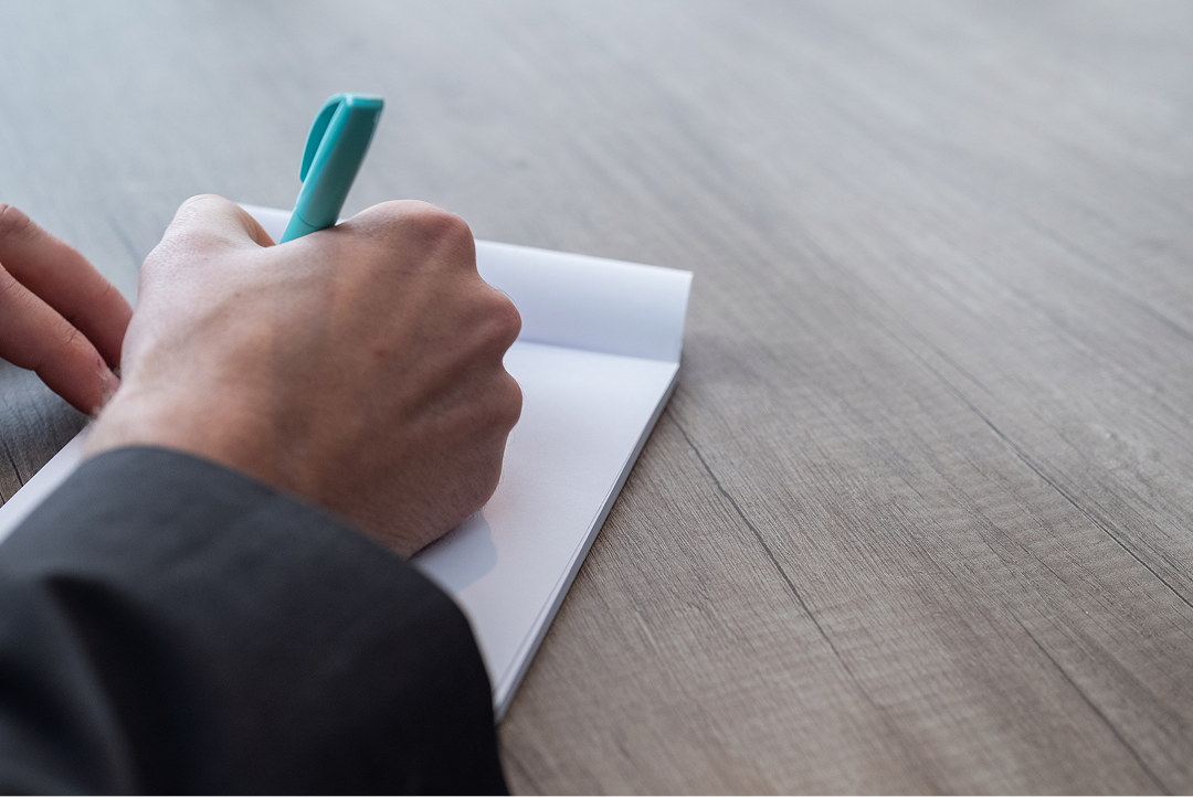 Close-up of a hand writing notes on a pad at a desk