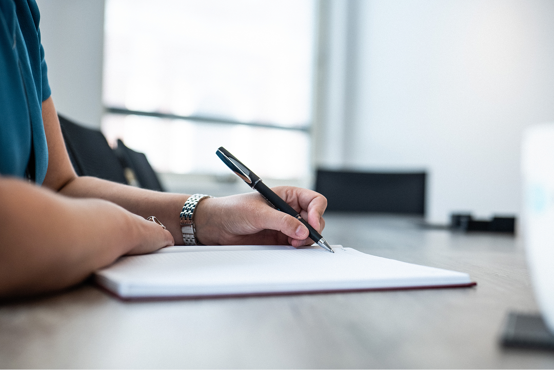 Close-up of a hand writing in a notebook at a conference table