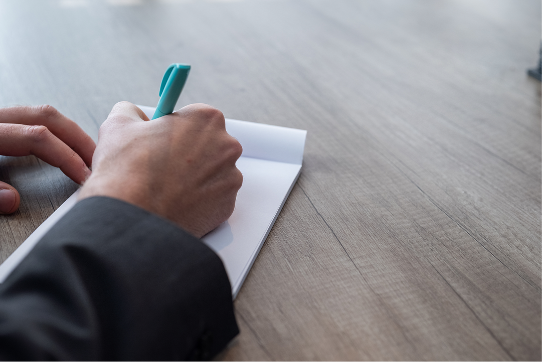 Close-up of a hand writing notes with a pen at a desk