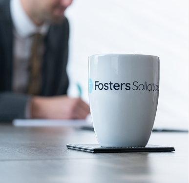 Fosters Solicitors mug on a table with a client in a suit in the background