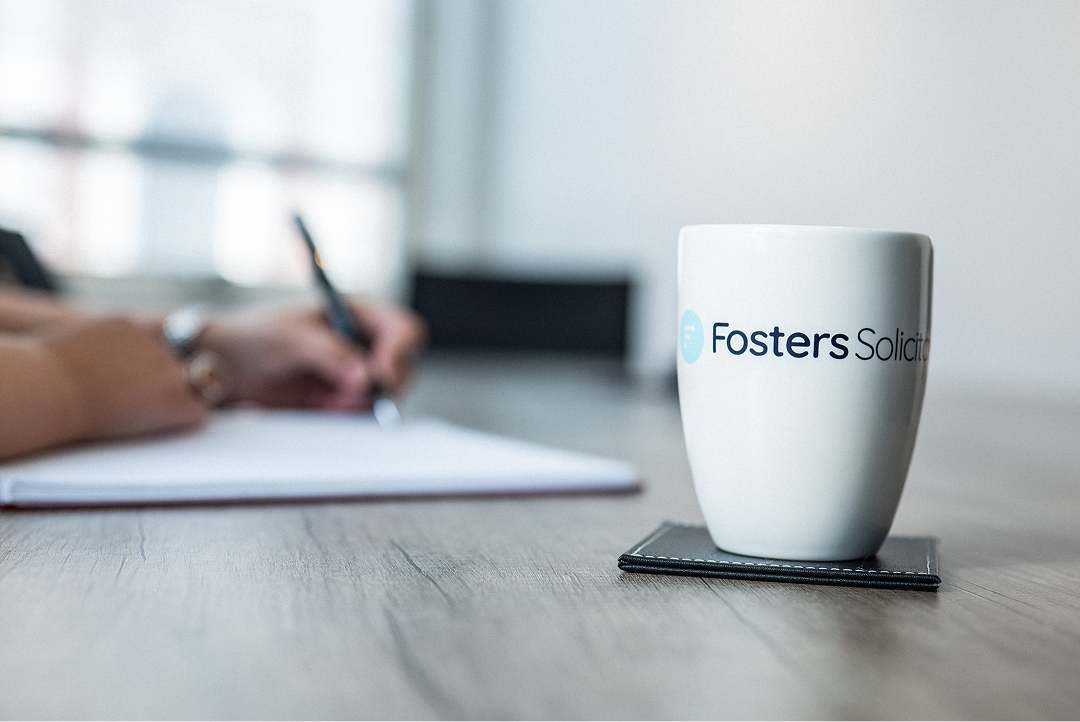 Fosters Solicitors mug on a table with a person writing in the background