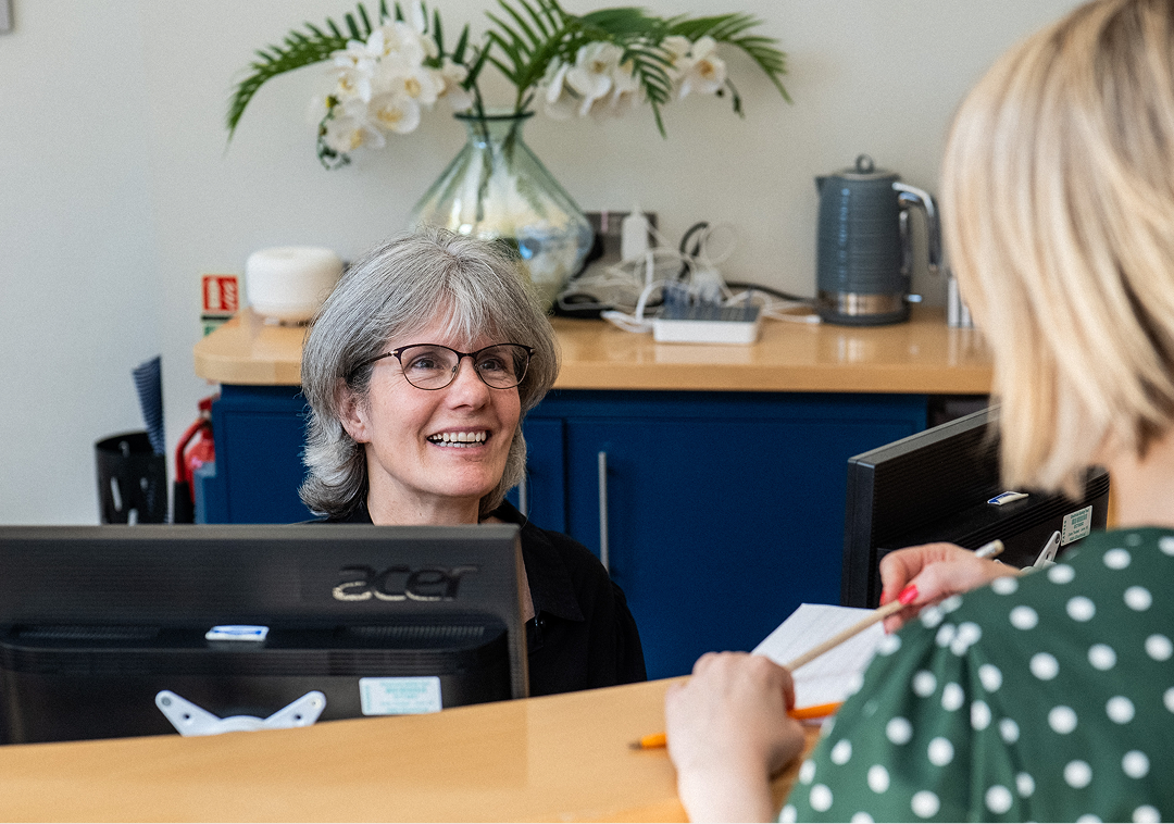 Fosters Solicitors receptionist assisting a client at the front desk with orchids in the background