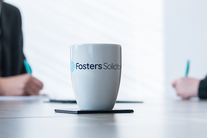 Fosters Solicitors mug on a desk with clients writing in the background